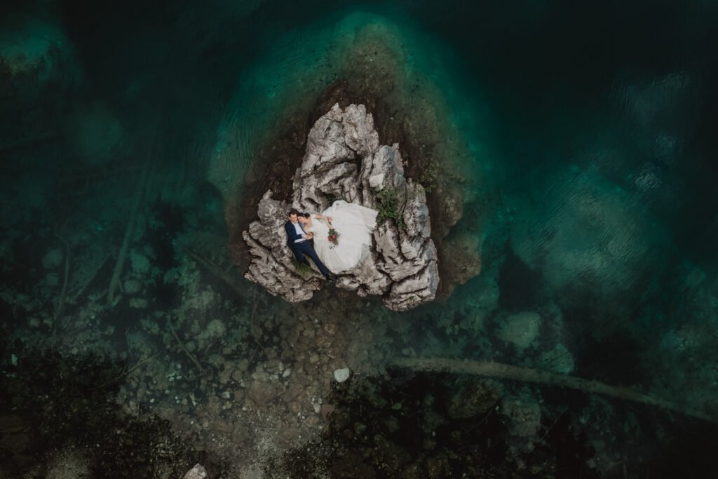 Aerial view of a couple on a small rocky island in turquoise water.