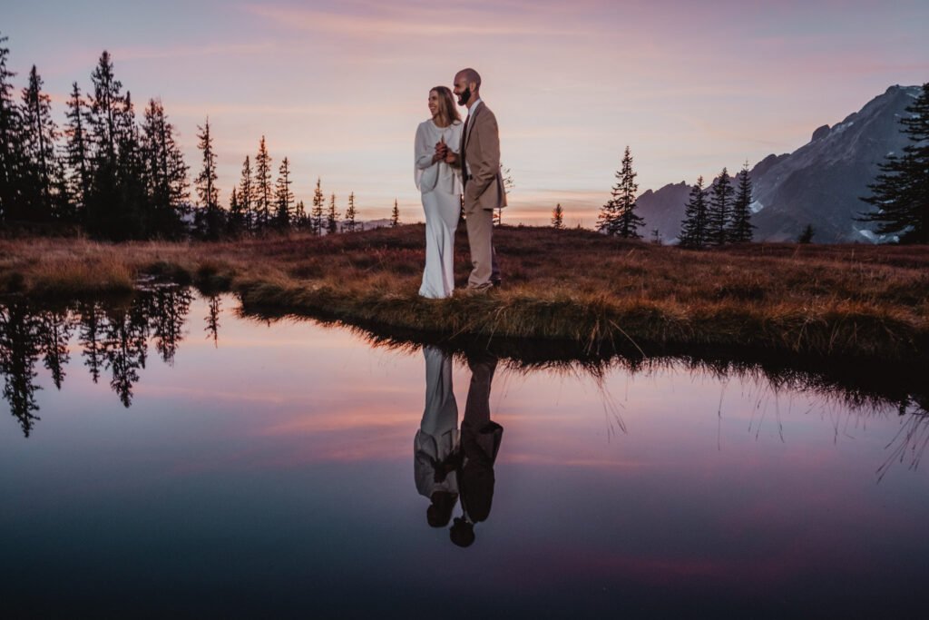 Couple embracing beside a pond reflecting the pink evening sky.