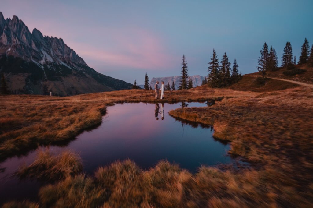 Couple reflected in a pond beneath the pink sunset.