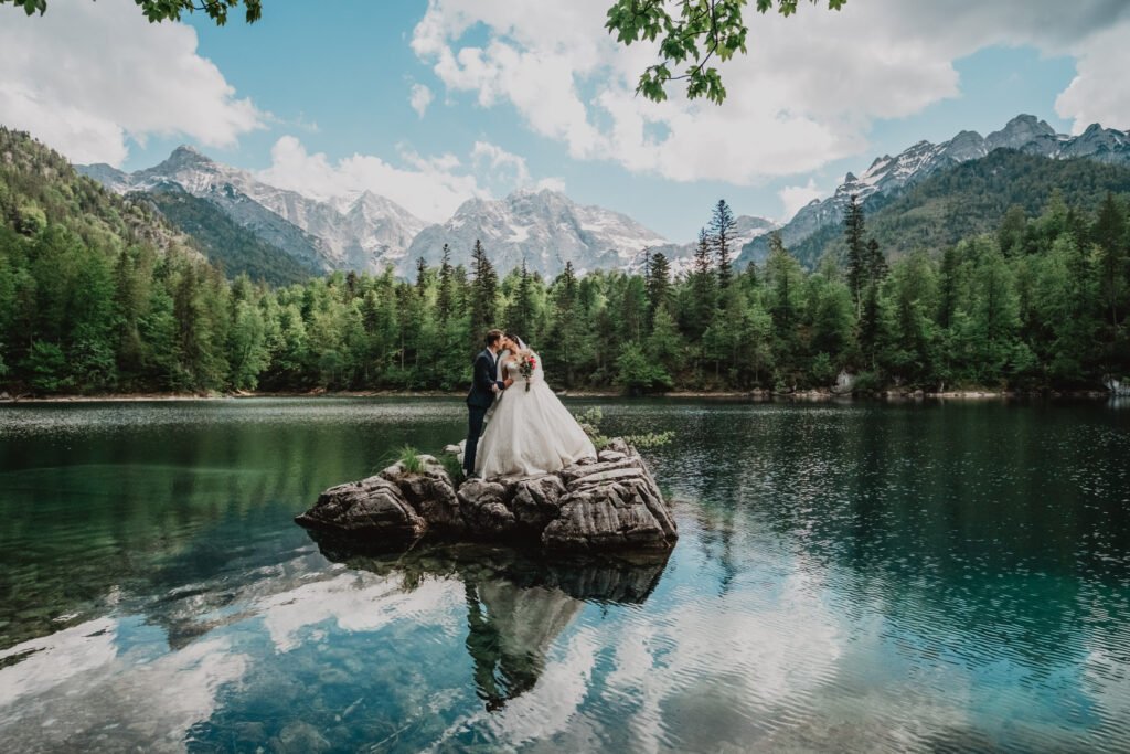 Bride reflected in the still water of a lake beneath mountain peaks.
