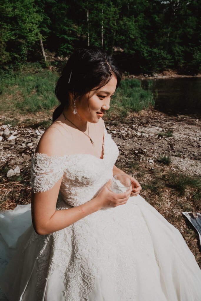 Bride adjusting her dress beside a mountain lake.