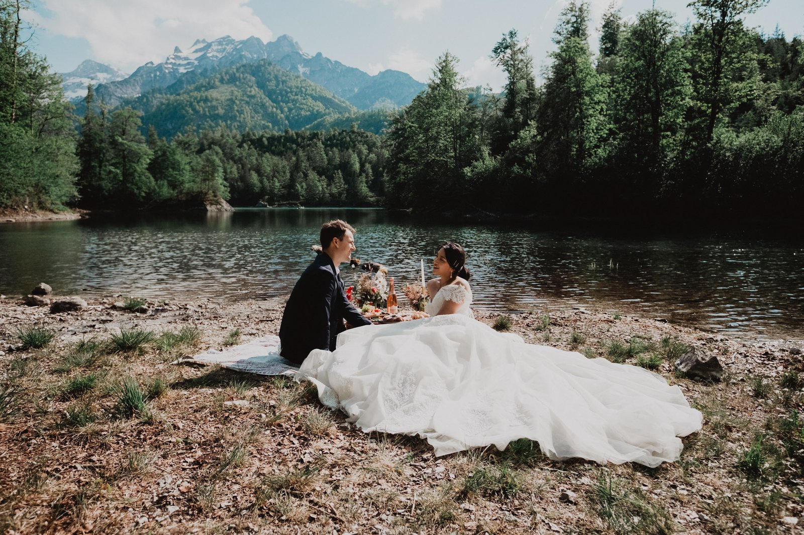 Braut und Bräutigam sitzen beim Picknick an einem Bergsee zusammen.