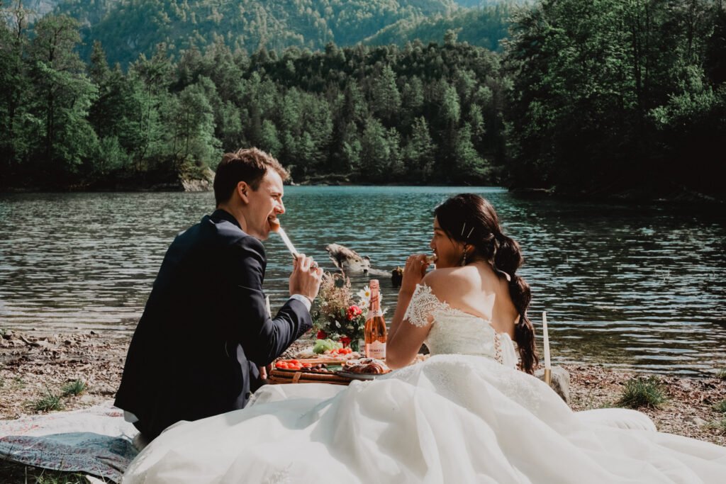 Couple smiling at each other over a lakeside picnic.