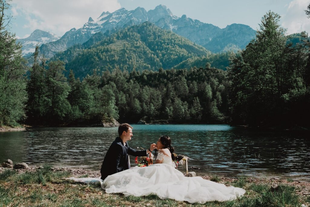 Couple sitting beside a forest lake with mountains in the distance.
