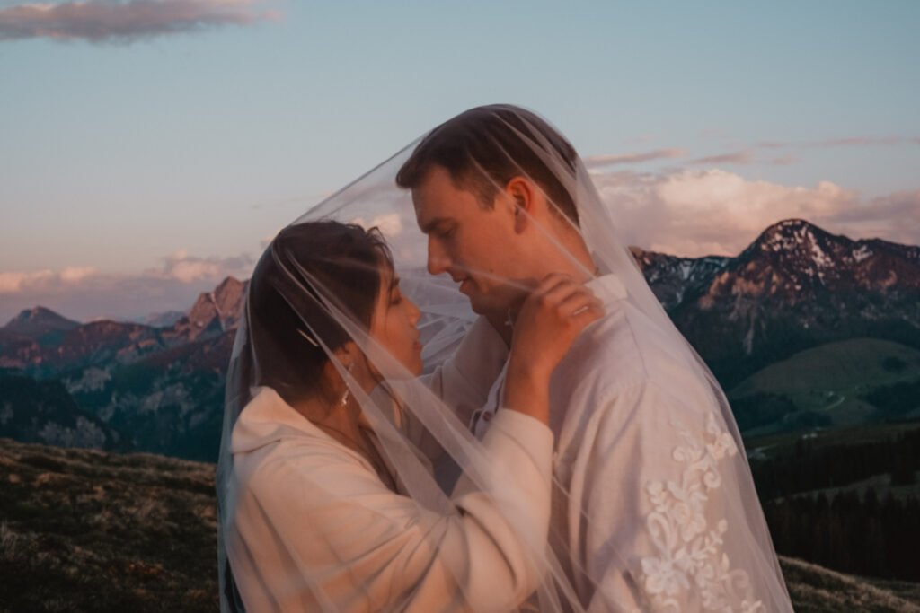 Couple facing each other beneath a veil at dusk in the mountains.