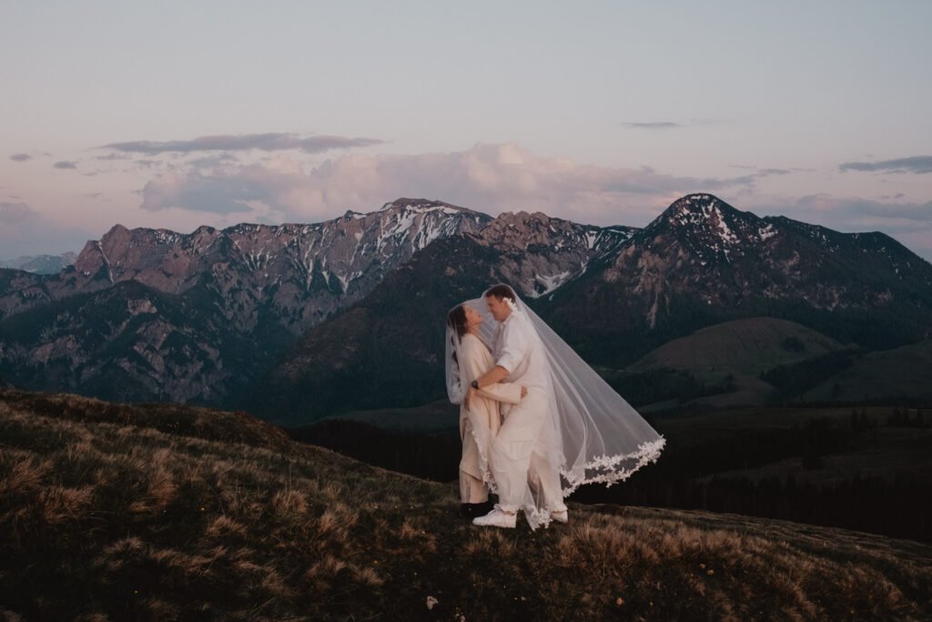 Couple kissing beneath a veil with a mountain range behind them.