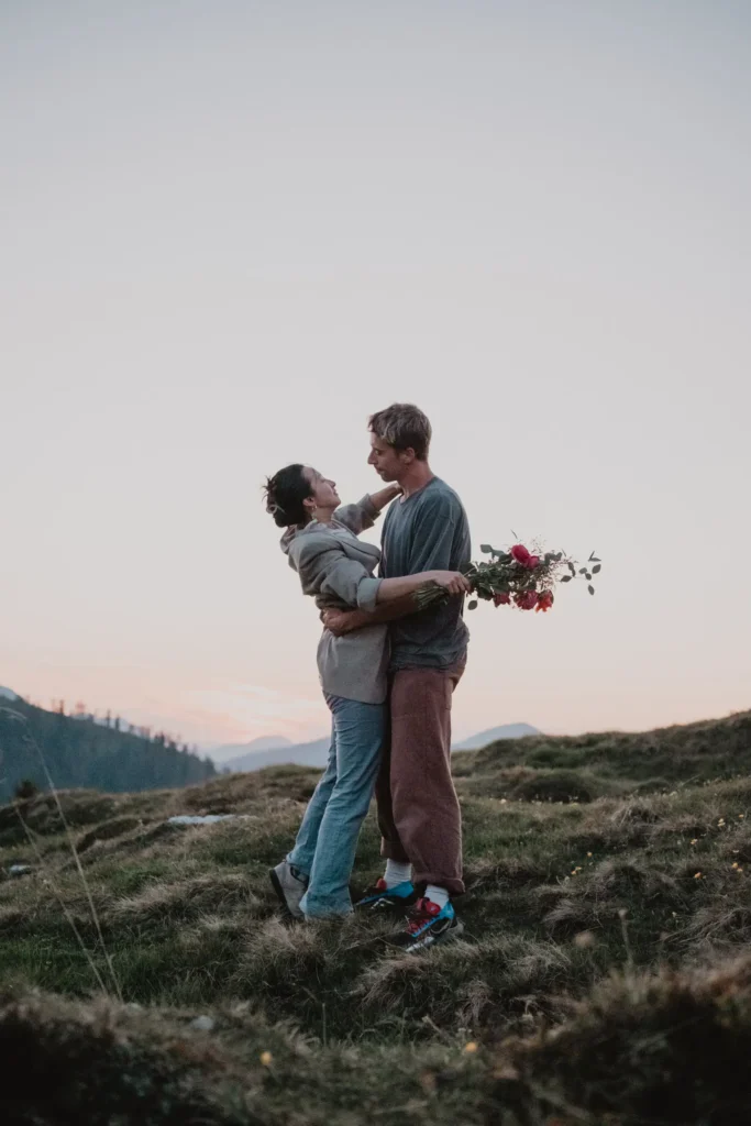 Couple embracing on a grassy mountain slope.