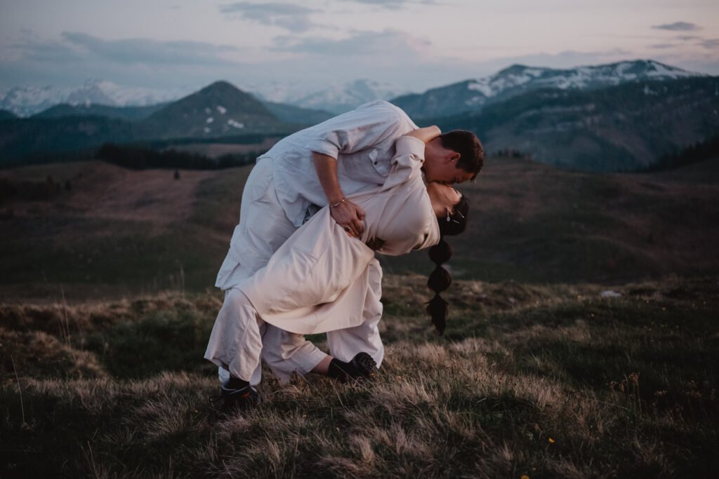 Groom dipping the bride during a playful moment on a mountain plateau.