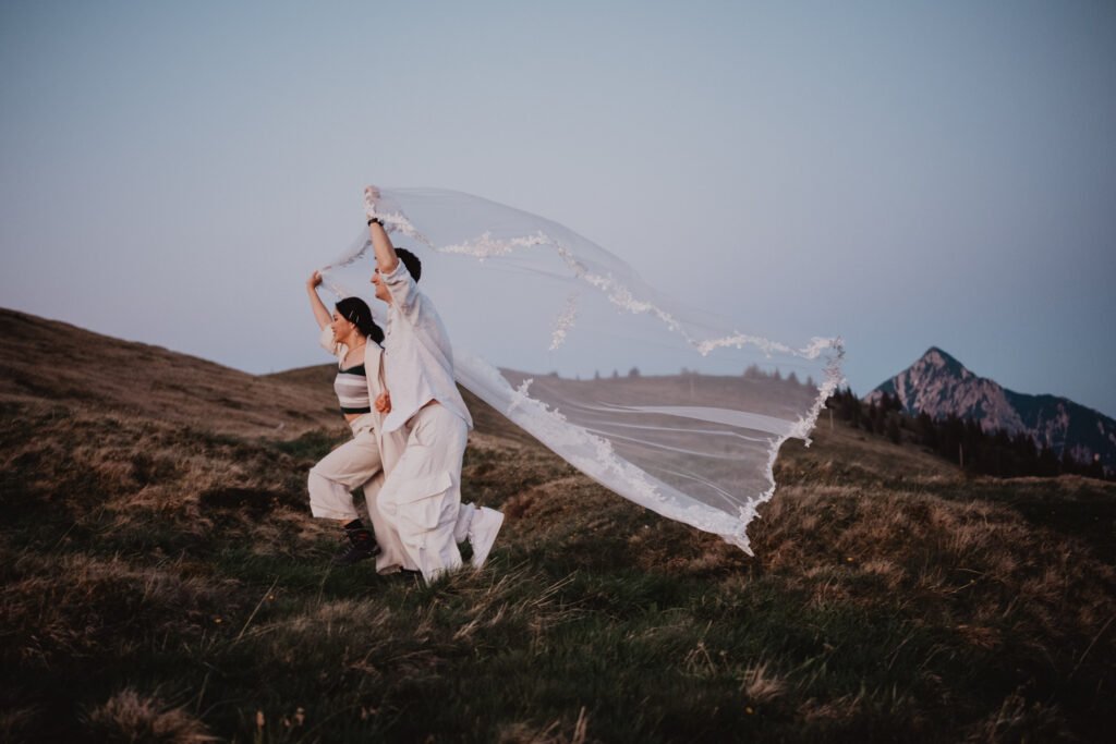 Bride lifting her veil as it streams across a mountain slope.