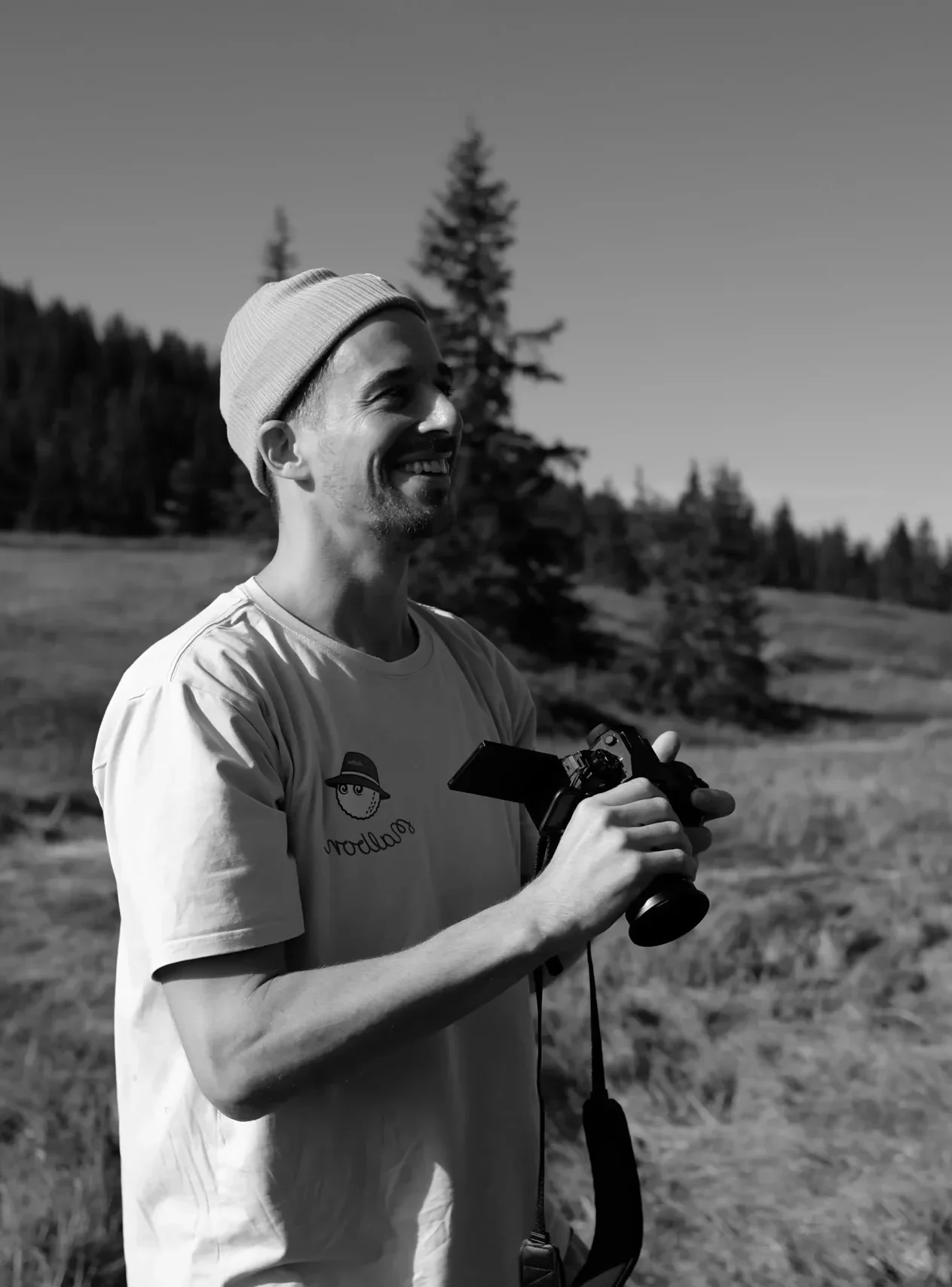 Elias smiling with his camera in an alpine meadow.
