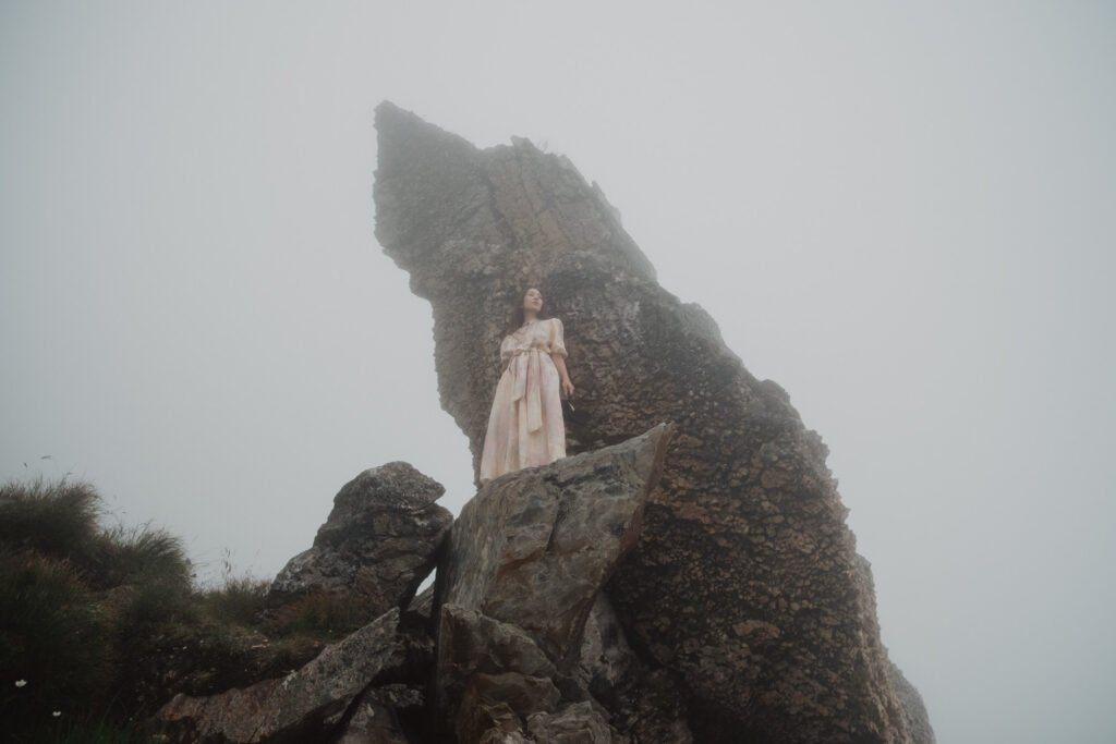 Bride standing beside a dramatic rock formation surrounded by fog.