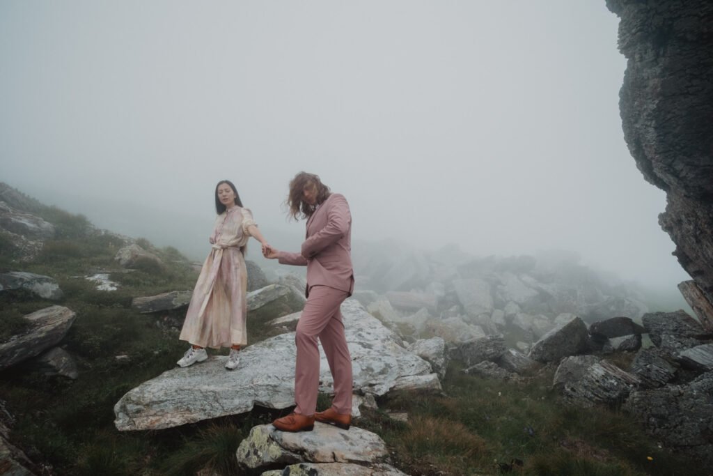 Couple facing each other on a rocky path in dense mountain mist.