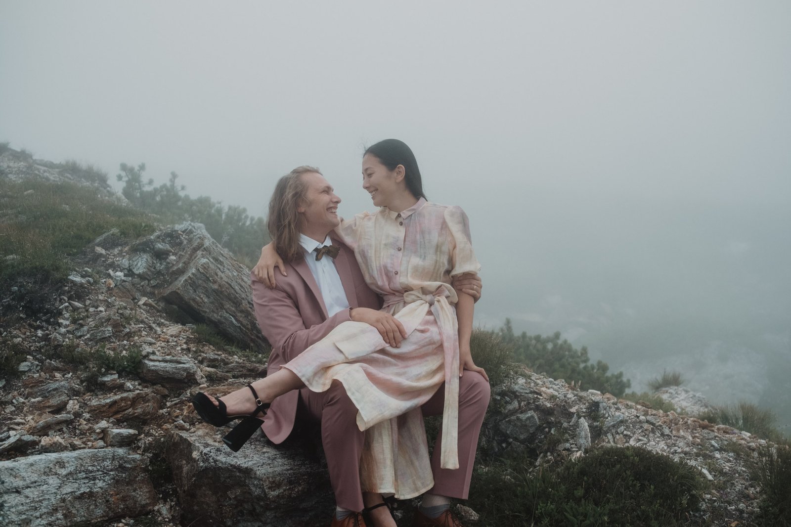 Paar sitzt lachend auf Felsen im Nebel.