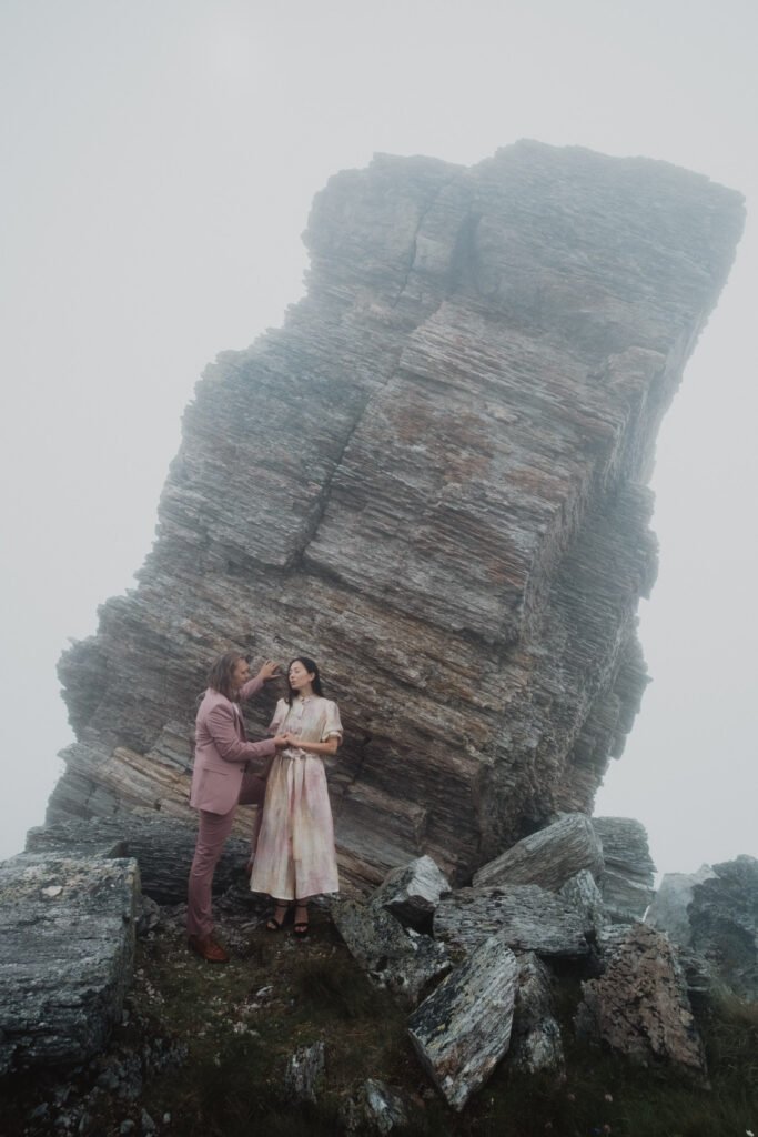 Couple standing beside a tall rock formation in mountain mist.