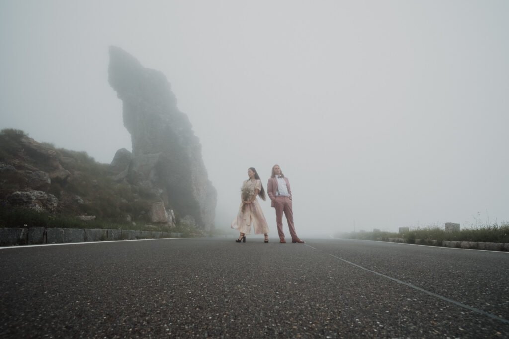 Couple standing beside a winding mountain road in the fog.