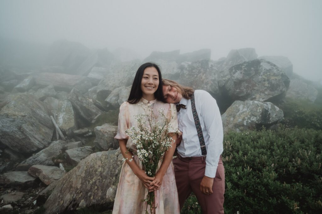 Bride holding a bouquet while her partner rests his head on her shoulder.
