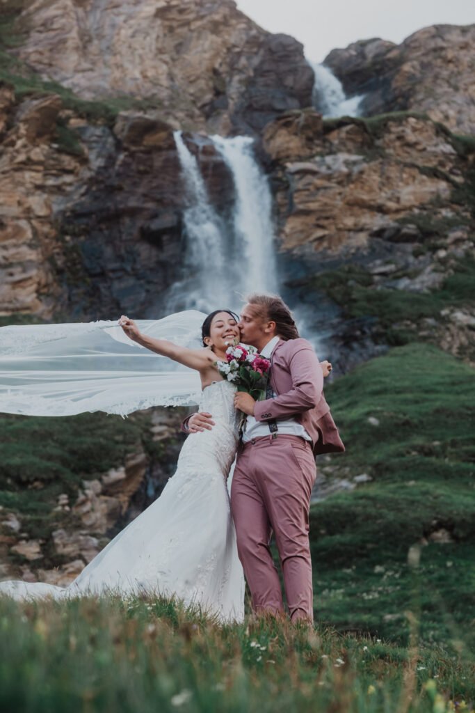 Couple celebrating beneath a waterfall with the bride's veil lifted in the air.