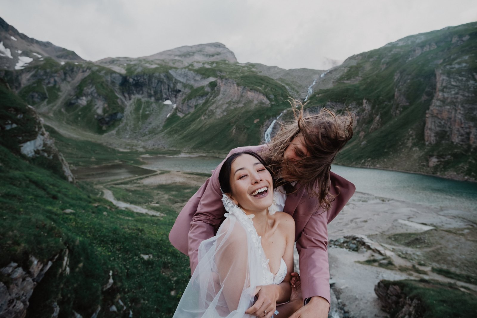 Couple laughing together above an alpine lake and waterfall.
