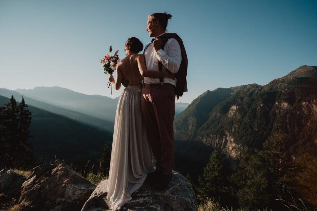 Couple standing together above a mountain valley in warm sunlight.