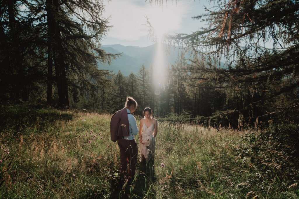 Couple walking through a sunlit meadow among mountain trees.