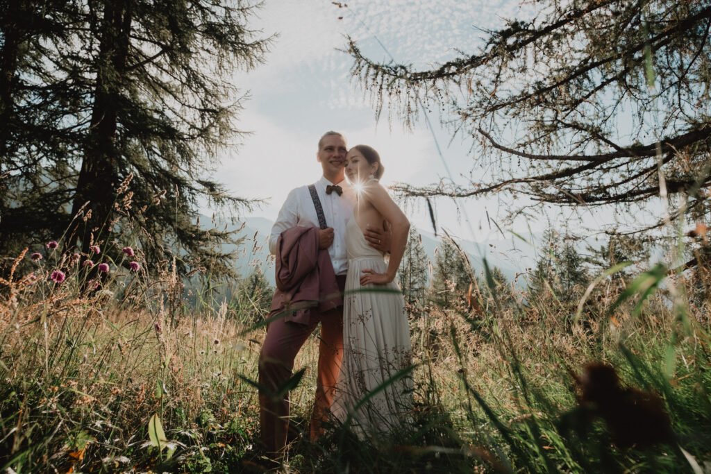 Couple walking through a sunlit clearing among alpine trees.