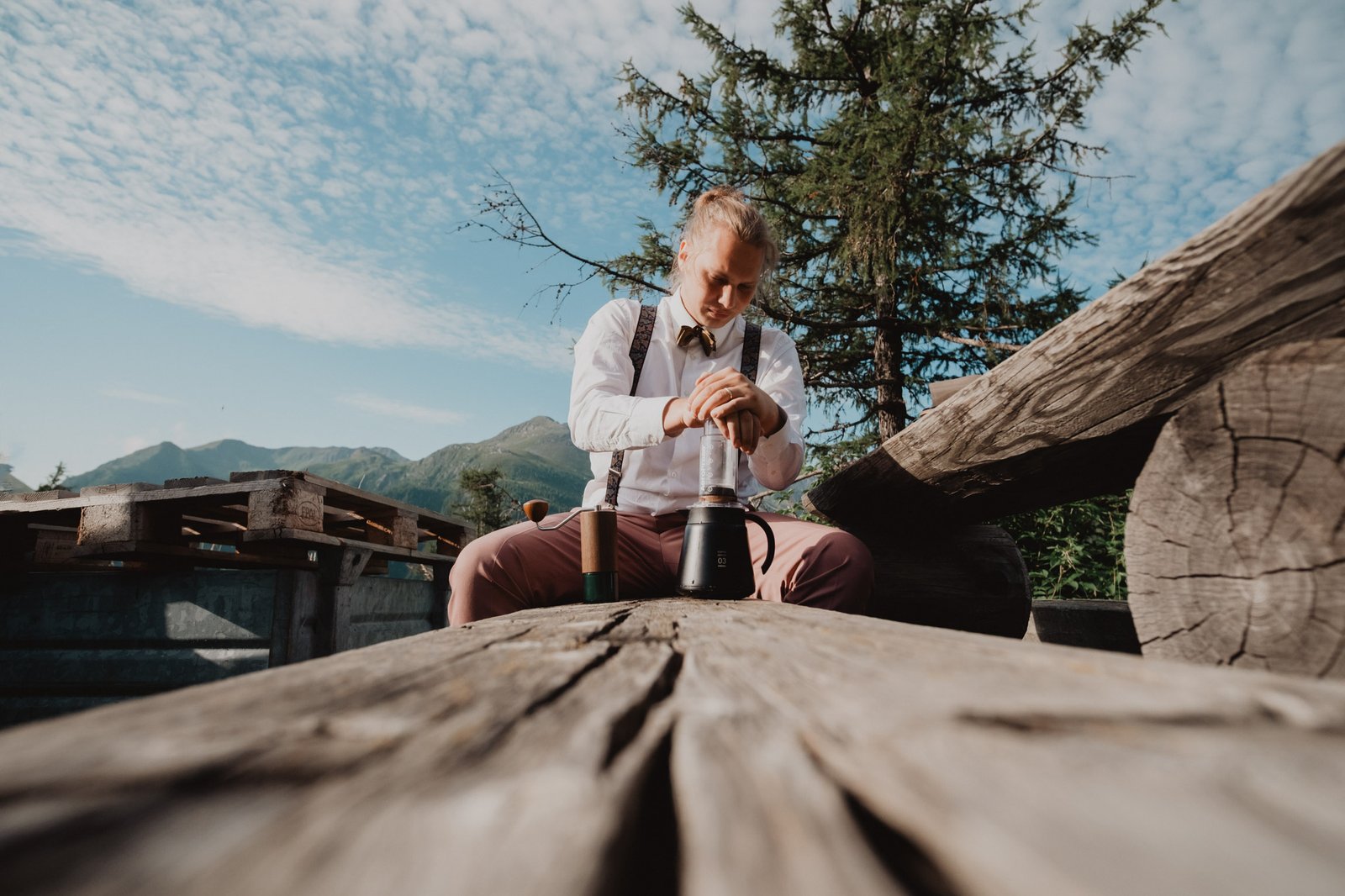Bräutigam sitzt neben einem hölzernen Picknicktisch in den Bergen.
