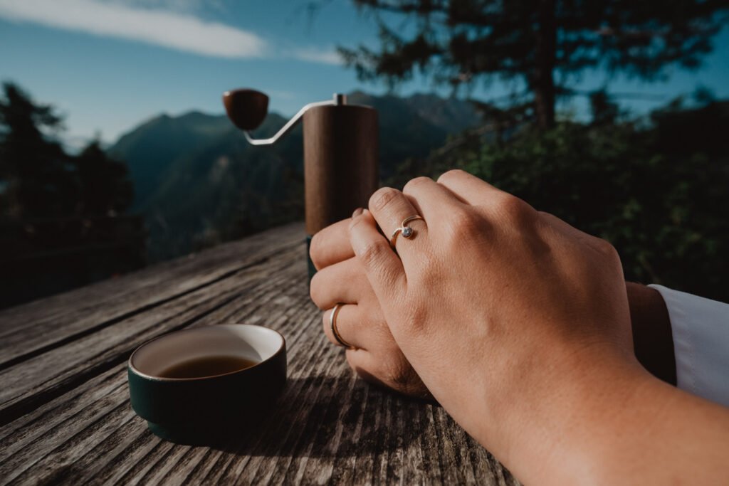 Close view of hands using a small coffee grinder on a wooden table.