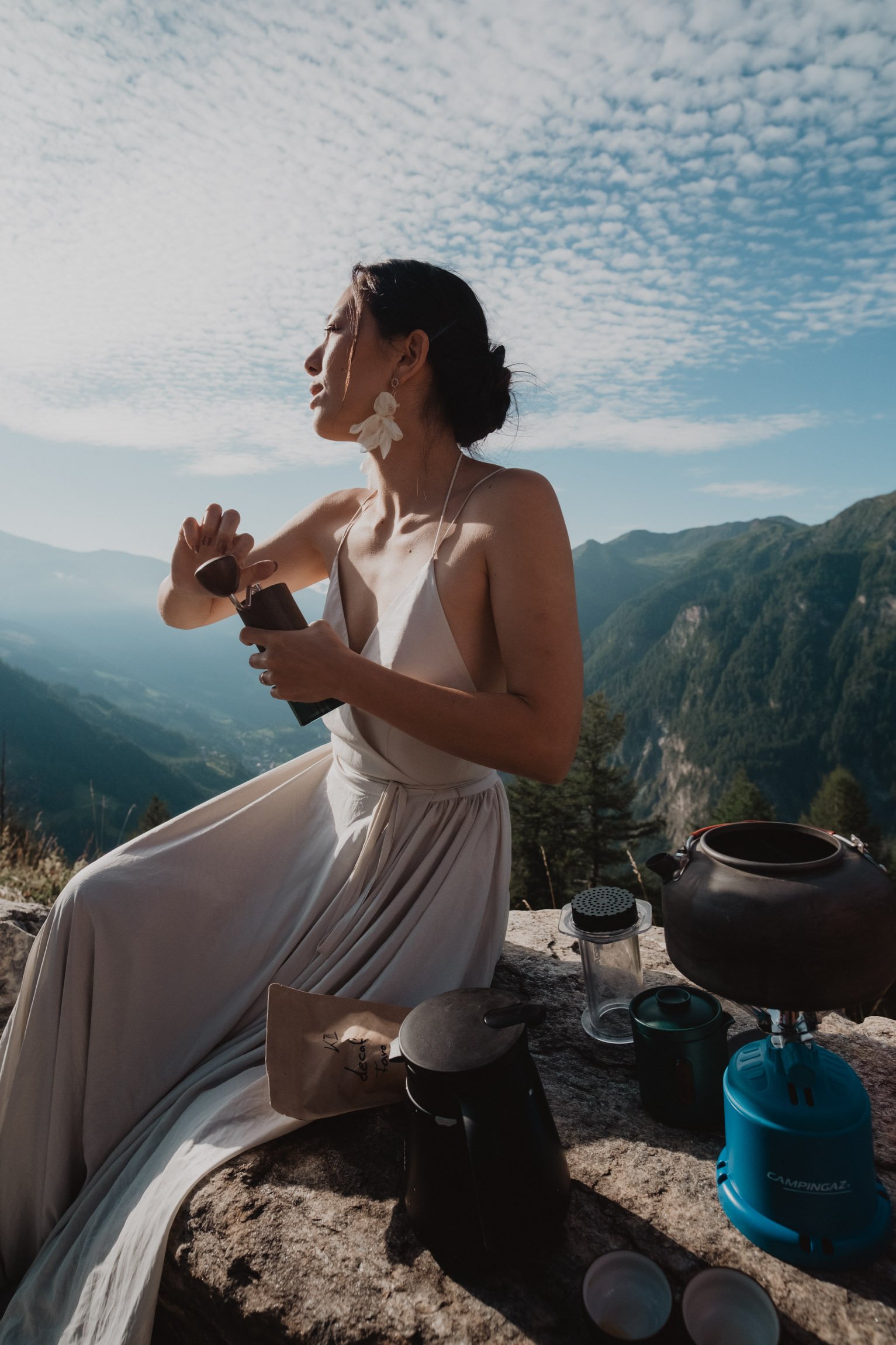 Braut genießt ein Getränk neben einem Picknicktisch in den Bergen.