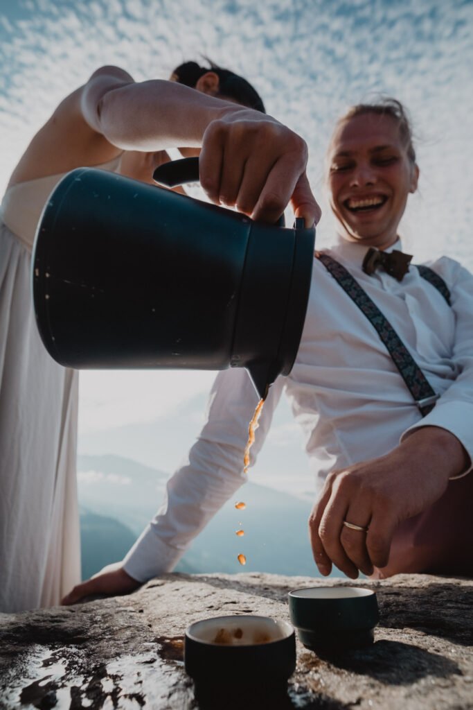 Groom pouring coffee outdoors at a mountain picnic table.
