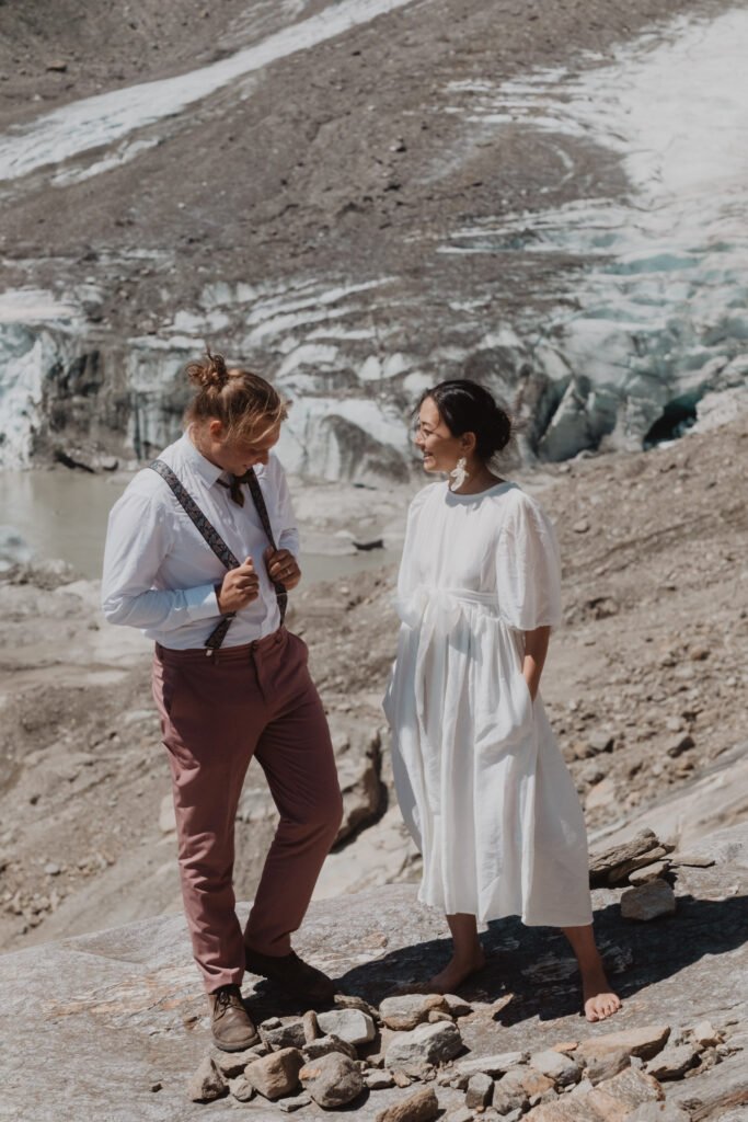 Couple standing together on rocky ground beside a glacier.