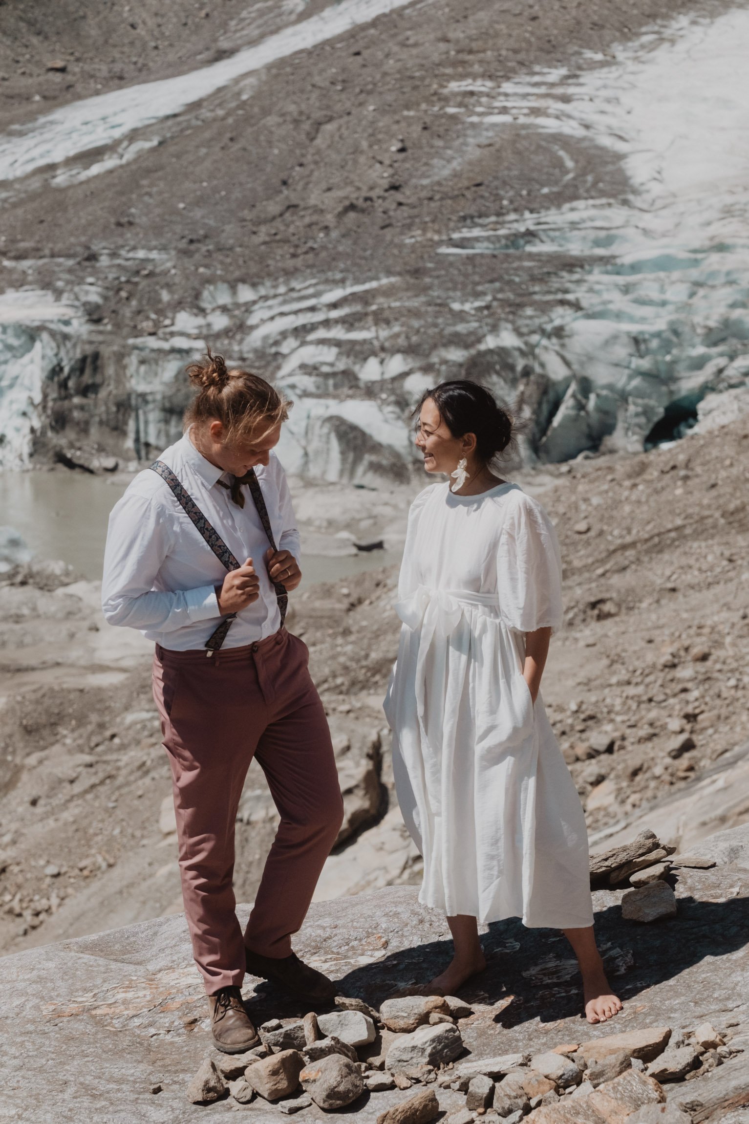 Couple standing together on rocky ground beside a glacier.