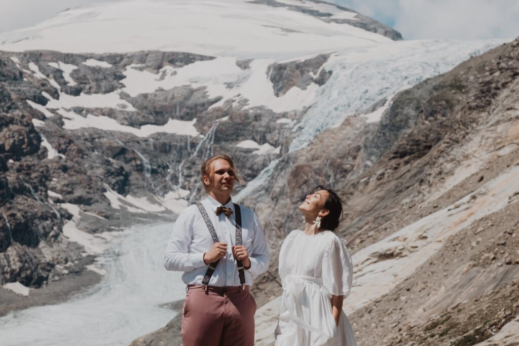 Couple laughing together against a glacier-covered mountain backdrop.