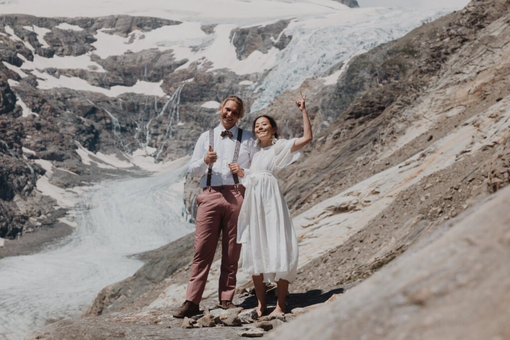Couple smiling and raising their arms in front of a glacier.