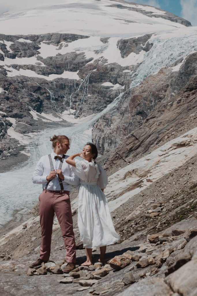 Couple walking beside rocky slopes beneath a glacier.