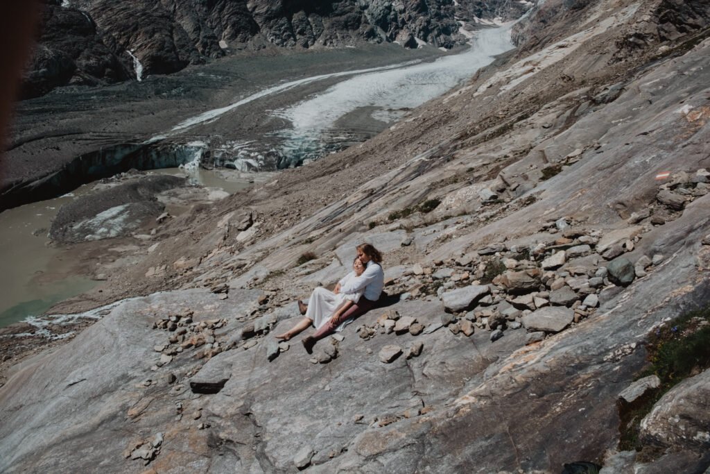 Couple sitting together on a rocky slope above a glacier.