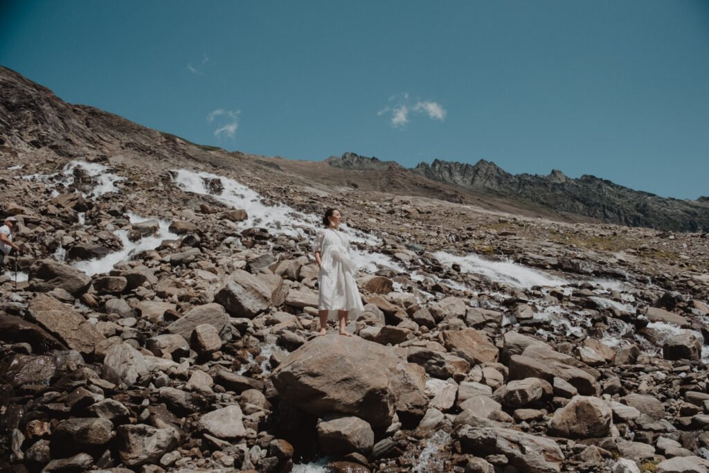Bride walking uphill across a rocky alpine slope.