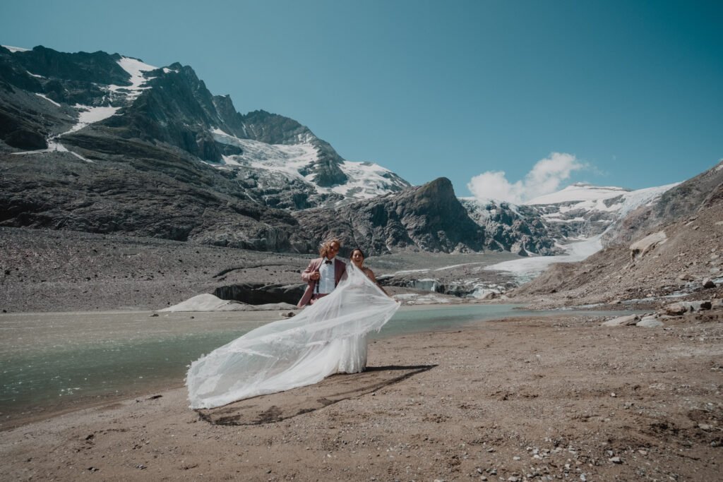 Bride's long veil flowing over rocks beside a glacier lake.