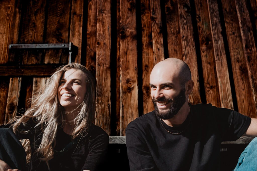 Couple laughing beside the wooden wall of a mountain hut.