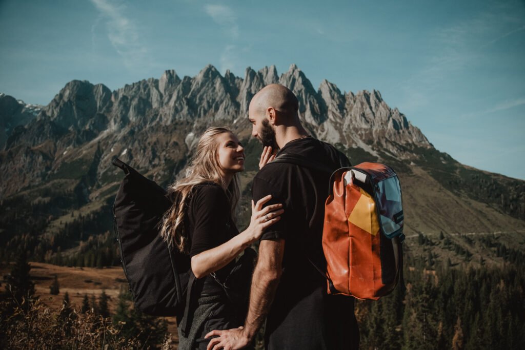 Couple embracing in the mountains, one wearing an orange backpack.