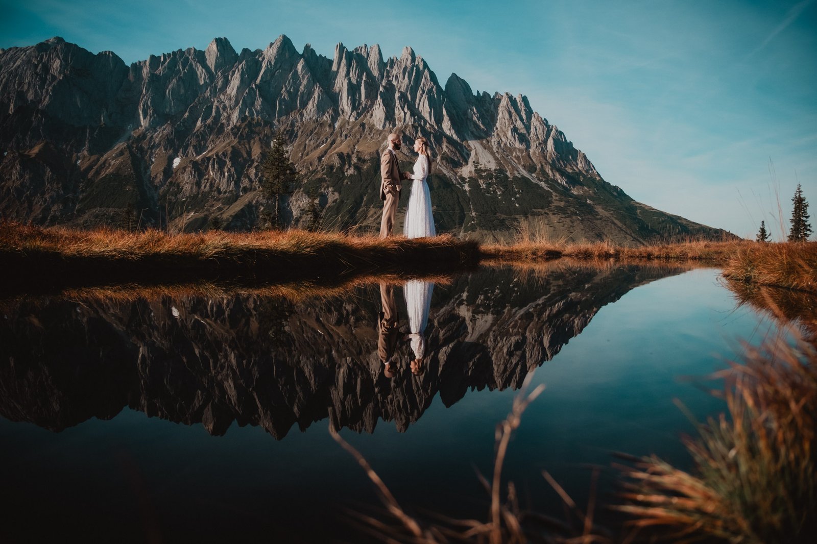 Paar spiegelt sich in einem von Berggipfeln umgebenen Teich.