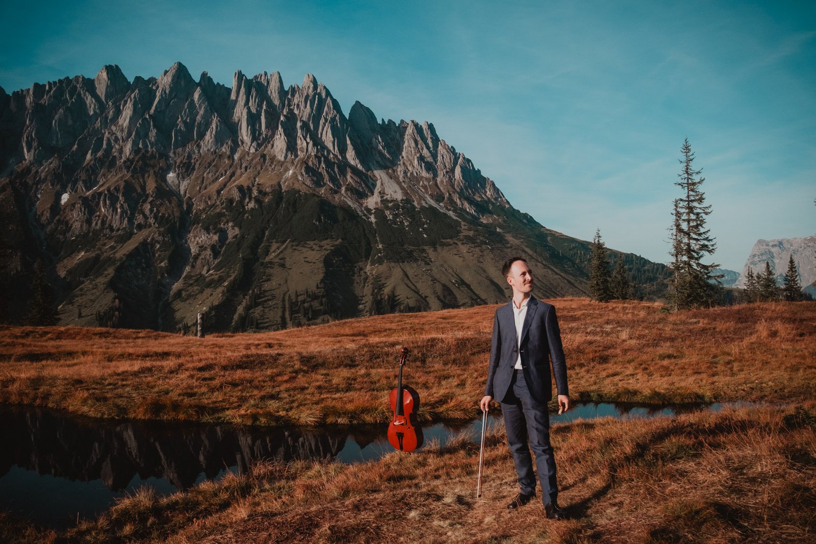 Cellist mit seinem Instrument neben einem Bergteich.