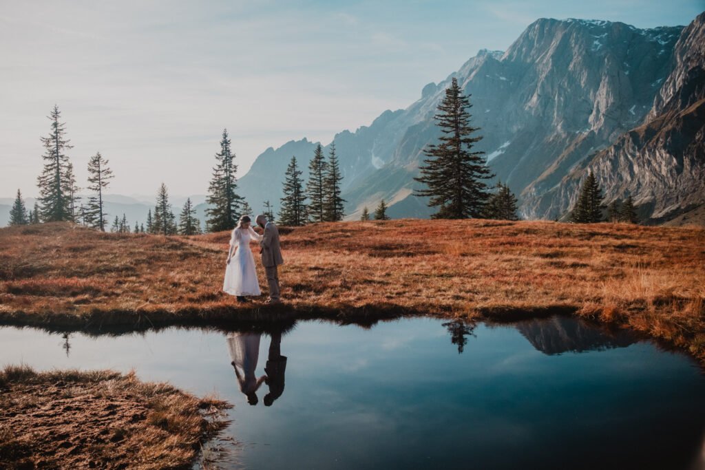 Couple and their reflection beside a mountain pond in daylight.