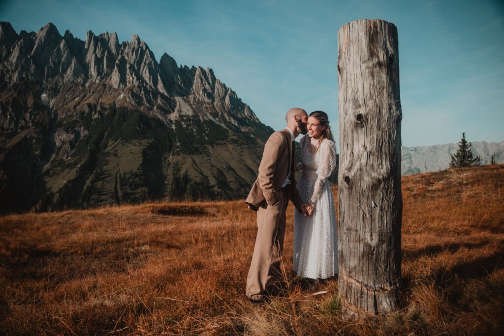 Couple leaning together beside a tall tree stump.