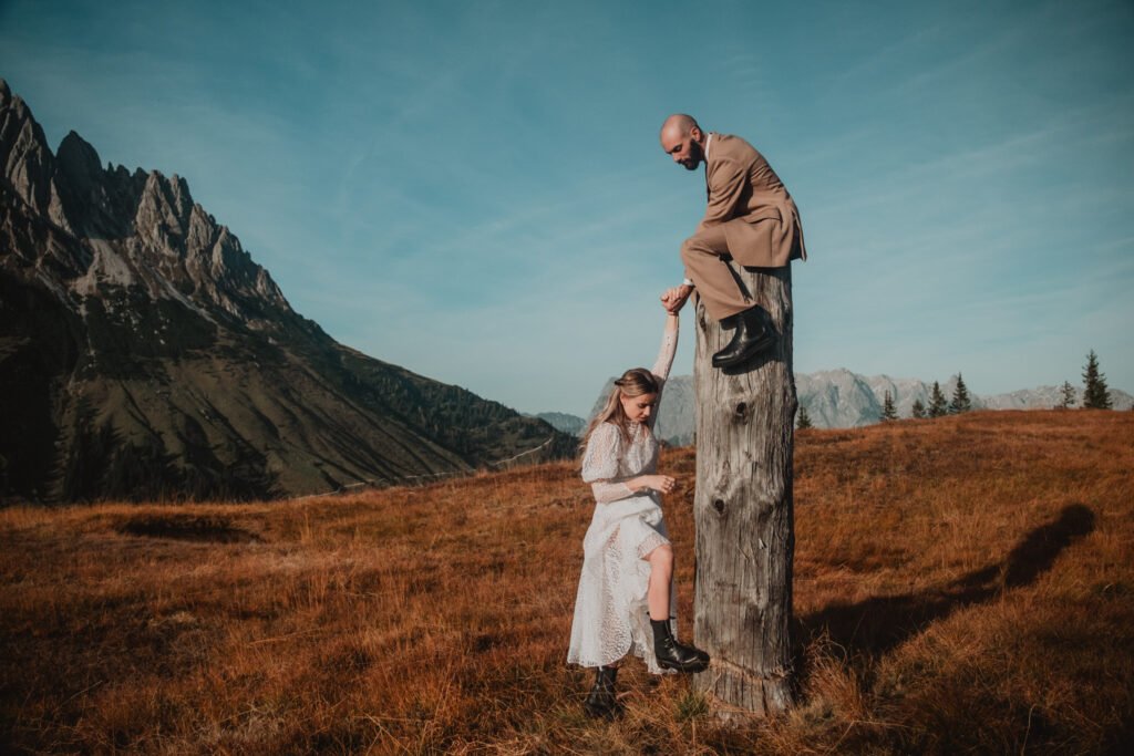 Bride standing beside the groom perched on a tree stump.