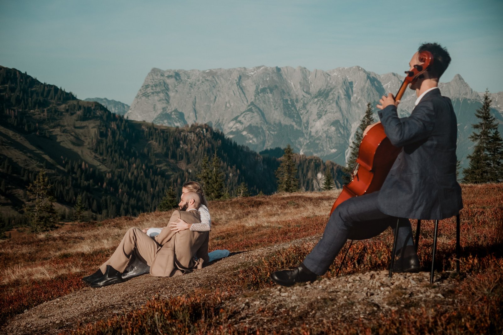 Cellist spielt neben einem Paar auf einer Bergwiese.