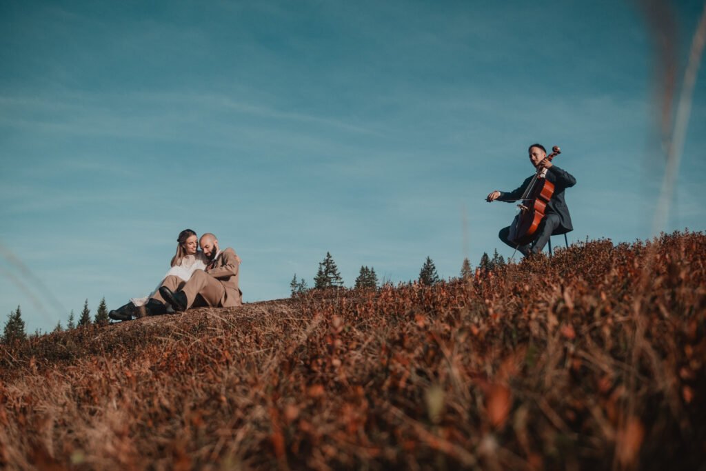 Paar und Cellist auf einer Wiese in der Berglandschaft.