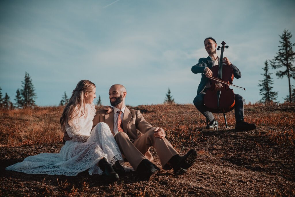 Couple sitting in a meadow with a cellist playing behind them.