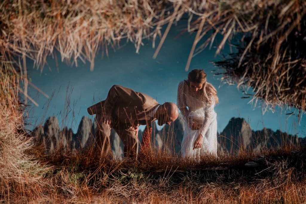 Couple leaning over a pond with their reflections below.