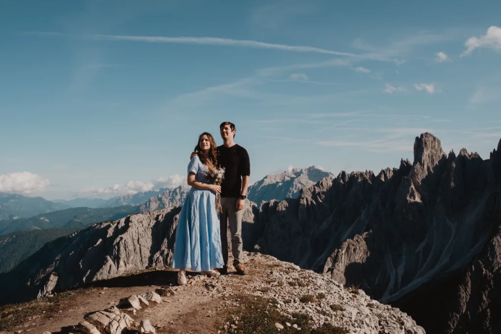 Couple standing together on a rocky summit, with a bouquet and jagged mountain peaks behind them.