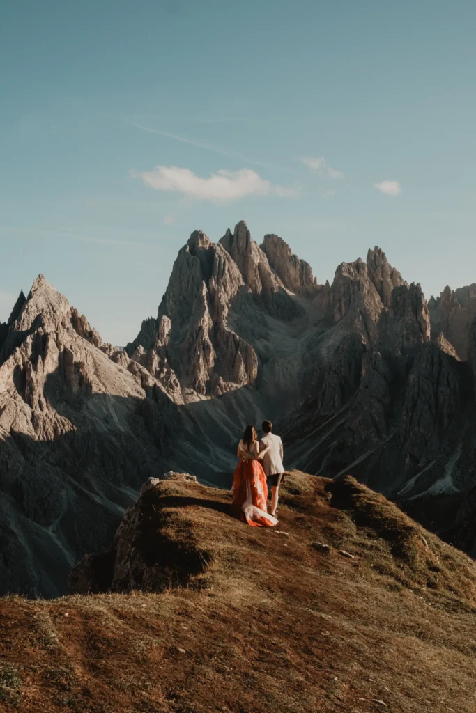 Couple standing on a ridge beneath jagged mountain peaks.